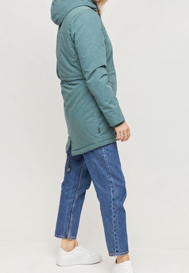 Parka esterna verde acqua, con texture e cappuccio, caratterizzata da una vita stretta, tasche laterali e cordoncino regolabile all'orlo. Indossata con jeans blu.
