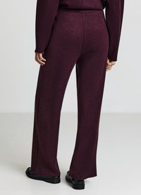 Bordeauxrote Hosen mit weitem Bein aus weichem Stoff. Sie haben eine hohe Taille, klare Linien und eine leichte Struktur. Der Saum endet knapp über eleganten schwarzen Schuhen.