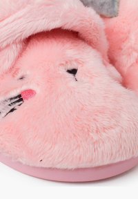 Puchate różowe kapcie o miękkiej fakturze, z wzorem przedstawiającym kreskówkową twarz. Podeszwa jest różowa i ma czarne oraz różowe akcenty.