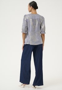 Světle fialový top s metalickými zlatými vzory, vycpanými rukávy a peplum pasem, v kombinaci s širokými tmavě modrými džíny a bílými lodičkami.