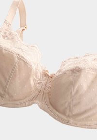 Beige bh med prikket stof og blondertrim. Har bøjler, justerbare stropper og en sløjfedetalje i midten. Glat tekstur generelt.