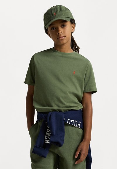 T-shirt verde-oliva com um pequeno logo bordado, emparelhada com calças verdes-oliva e um casaco de moletom azul-marinho atado à cintura.