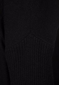 Primo piano di un tessuto nero lavorato a maglia che mostra una texture a coste e dettagliati motivi di cucitura.