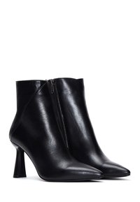 Bottes basses en cuir noir avec un bout effilé et un talon pointu. Caractérisées par une texture brillante et une fermeture éclair latérale.