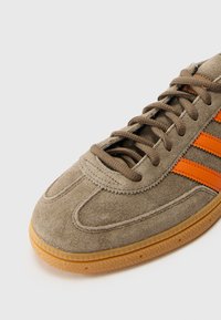 Pruun nubukist sneaker oranžide triipudega, ümar varvas ja tekstureeritud kummitald. Omab lipsuga sulgemist ja pehmendatud krae mugavuseks.