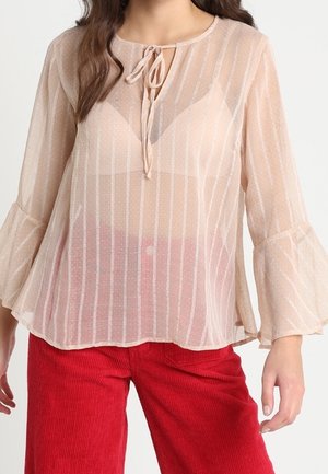 Blusa trasparente di un leggero pesca con righe verticali, colletto con fiocco e maniche lunghe svasate, abbinata a pantaloni in velluto a coste rossi.