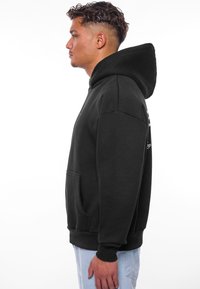Sort hættetrøje lavet af blødt materiale, med en kængurulomme, ribbede manchetter og en stor hætte. Moderne pasform med minimalistisk design.