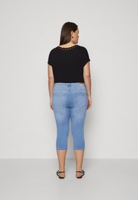 Svart topp med kort erme og bølget halslinje, kombinert med lyseblå caprijeans. antrekket har et enkelt design og en figurnær silhuett.