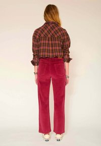 Chemise en flanelle à carreaux dans des tons de violet et de vert, associée à un pantalon en velours côtelé rouge taille haute. Design à jambes larges avec poches arrière, portant des chaussures en toile.