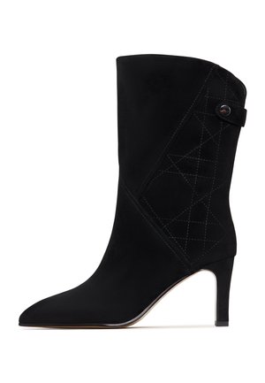 Schwarze Wildleder-Ankle Boots mit spitzer Zehe, schmalem Absatz und gestepptem geometrischem Design an der Seite. Mit einem Knopfdetail am Knöchel.