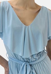 Ljusblå klänning av mjukt tyg med djup V-ringning, volangärmar och midjeband, med plisseringar på kjolen.