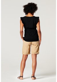 Haut noir à volants avec taille cintrée, associé à un short beige roulé. Des sandales plates noires complètent cette tenue décontractée.