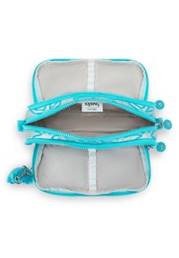 Kipling pengekat i turkise stof med to lynlåslommer, mesh-opdelinger og en fluffy blå charm hængende ved.