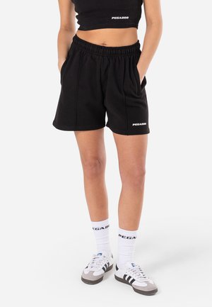Shorts en polaire noire avec une taille élastique, des poches latérales et un logo "PEGADOR" discret à l'ourlet. Associés à des chaussettes montantes blanches et des baskets.