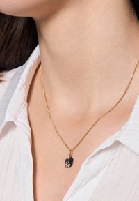 Złoty naszyjnik z łańcuszkiem z sercowym, czarnym wisiorkiem z wzorem łapki. Łańcuszek jest cienki, a wisiorek ma wyraźny kształt.