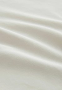 Puha, világos bézs színű szövet finom redőkkel és finom, sima szövött textúrával, közelről bemutatva.