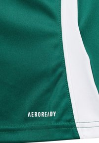 Tela atlética verde con acentos laterales blancos, que presenta tecnología de absorción de humedad. Texto "AEROREADY" en blanco en una costura. Textura suave.