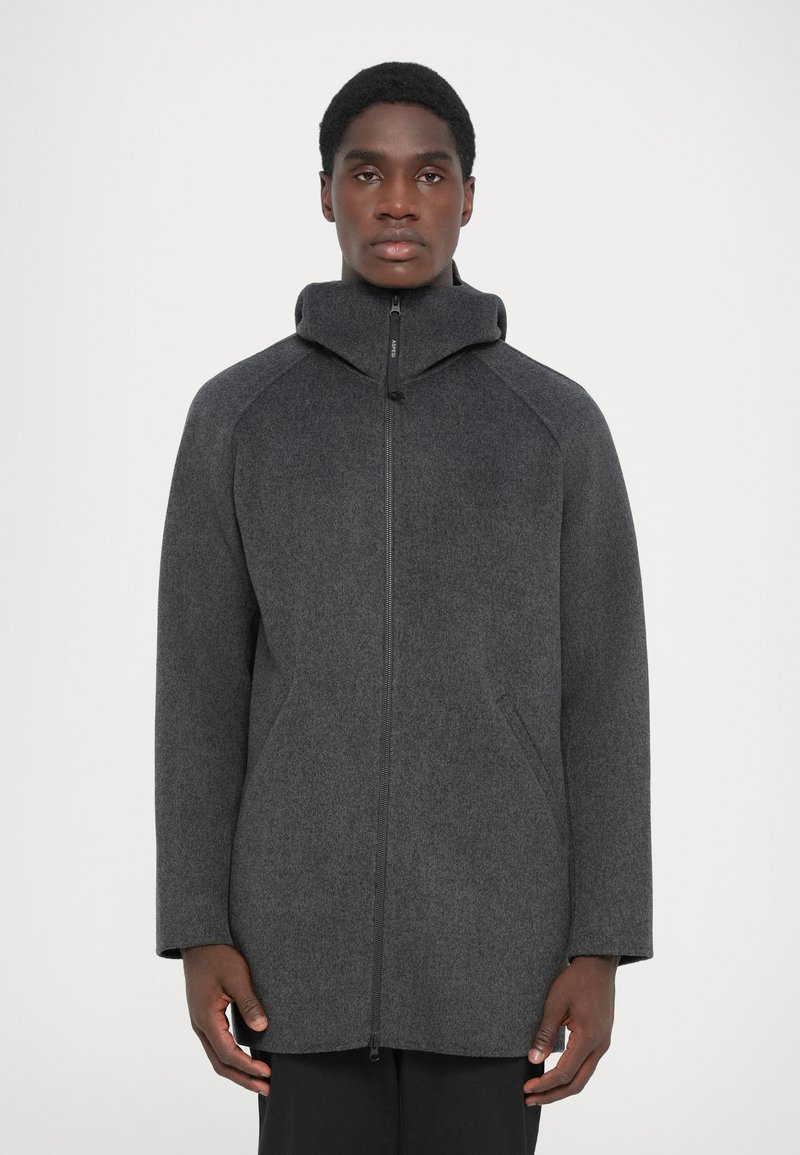 Dark gray wool coat with a high collar, side pockets, and a front zipper closure. Features a relaxed fit and textured fabric.
