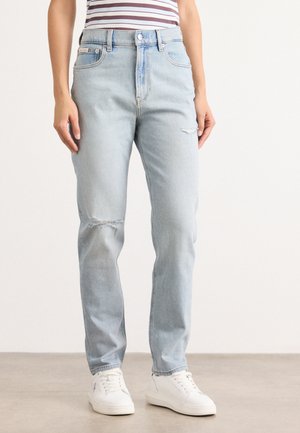 Lichtblauwe denim jeans met een hoge taille, een relaxte fit en scheuren bij de knieën. Voorzien van vijf zakken en metalen accessoires. Gepaard met witte sneakers.