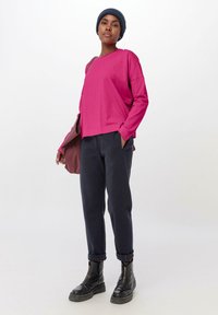 Růžový top s dlouhým rukávem a uvolněným střihem, ve spojení s námořnickými jogger kalhotami. Doplněno tmavým čepicovým kloboukem a černými robustními botami.