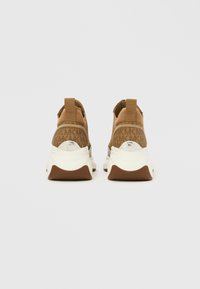 Rjavi športni copati z zgornjim delom iz teksturirane tkanine, vzorcem logotipa na zadnjem delu in belim gumijastim podplatom z rjavimi poudarki.