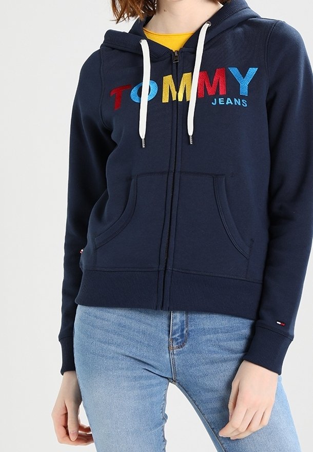 Navy zip-up hoodie made of cotton, featuring a front pocket, drawstring hood, and multicolored "TOMMY" logo across the chest.