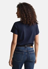 Navy blue short-sleeve t-shirt with a round neck, paired with dark denim jeans featuring a simple back pocket design and a brown leather tag.