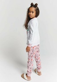 White long-sleeve shirt with colorful graphic, paired with pink pajama pants featuring Hello Kitty patterns. Slipper-like footwear completes the look.