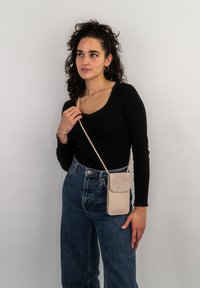 Beige crossbody bag with a rectangular shape, smooth texture, and a flap closure. Paired with a black long-sleeve top and high-waisted denim pants.