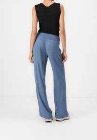 Svart ärmlös topp som matchas med ljusblå, flödande, vida byxor med smockad midja och texturerad väv.