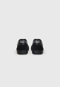 Sneakers pretos com uma mistura de texturas lisas e em camurça, com sola de borracha e logo "EA7" no calcanhar. Design simples e aerodinâmico.
