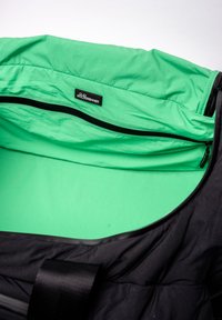 Sac de sport noir avec un intérieur vert vif, texture lisse, fermeture éclair double et une étiquette de marque visible à l'intérieur.