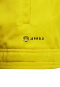 Gelbes Sportgewebe mit strukturierter Oberfläche, versehen mit dem gedruckten "AEROREADY"-Logo und einem Globussymbol in der Nähe des Saums, das die Leistungsmerkmale hervorhebt.