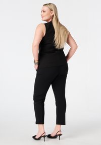 Zwarte mouwloze top met een getailleerde pasvorm, gecombineerd met zwarte slim-fit broek en zwarte sandalen met hak. Accessoires zijn onder andere opvallende oorbellen en armbanden.