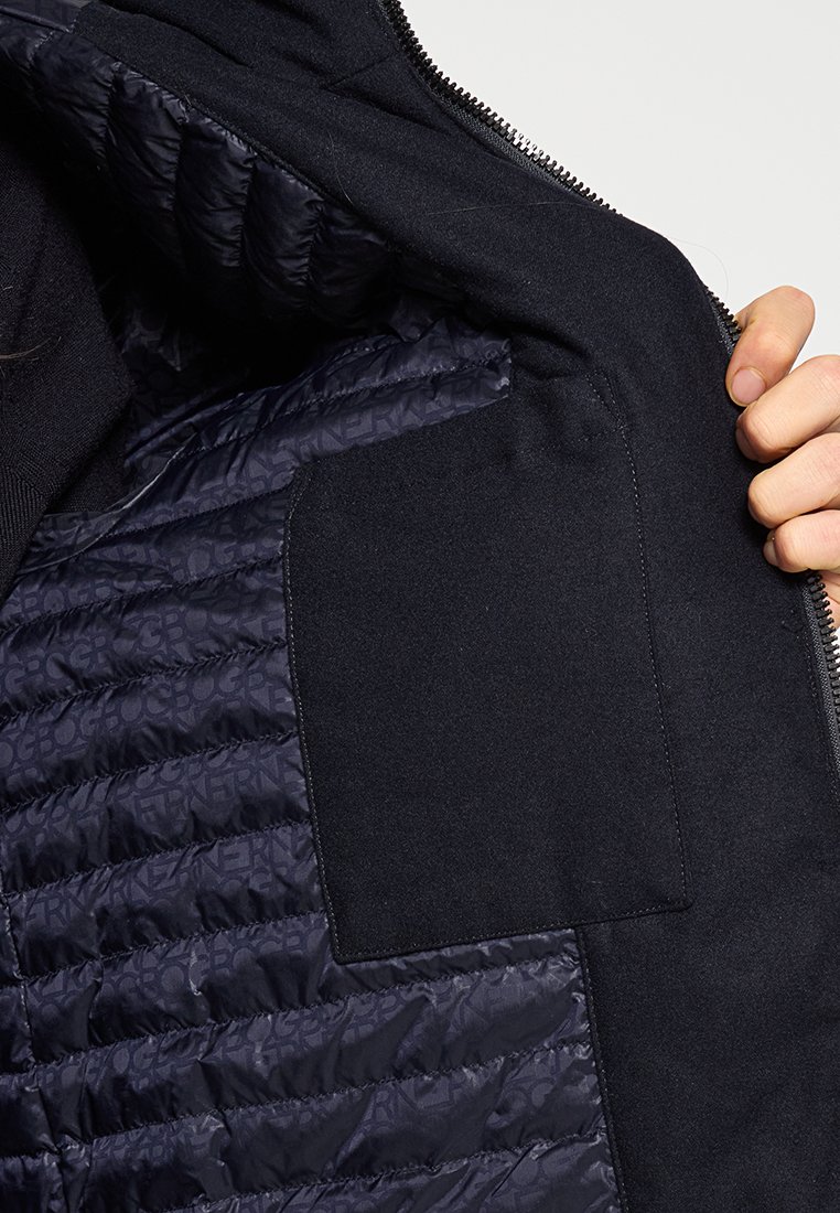 Das Innere einer Marinejacke zeigt auf der linken Seite einen gesteppten Stoff und auf der rechten Seite einen glatten Stoff, mit einer aufgesetzten Tasche und einem Reißverschlussdetail.