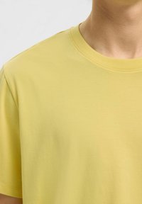 T-shirt jaune à manches courtes en coton doux. Il présente un col ras du cou et une texture lisse, avec un design simple et sans motifs visibles.
