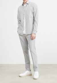 Camisa de botones a rayas en gris y blanco, superpuesta a una camiseta blanca básica. Pantalones ajustados gris claro y zapatillas blancas completan el look.
