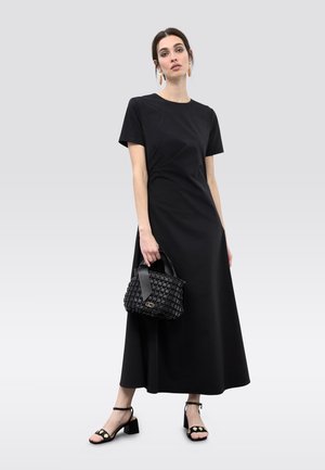 Vestido maxi negro de manga corta, textura suave. Incluye un bolso tejido negro con asa de cinta. Sandalias negras de tacón con adornos.