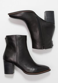Botas de piel negra hasta el tobillo con punta afilada, cremallera lateral y tacón de bloque apilado. Textura suave y acentos de costuras mínimas.
