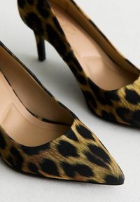 Läderskor med leopardmönster och hög klack, med spetsig tå, tillverkade av strukturerad textil, med en svart och guld färgskala och en smal stilettklack.