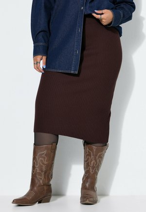 Una modelo lleva una chaqueta vaquera azul marino, una falda midi marrón de canalé, medias negras y botas vaqueras marrones bordadas.