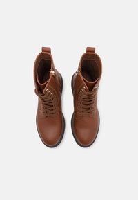 Bottes de cheville en cuir marron avec lacets, fermetures éclair latérales, bouts ronds et semelles noires, vues de dessus sur fond blanc.