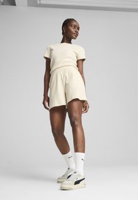 Tricou bej cu dungi și pantaloni scurți asortați, având un logo pe pantaloni. Șosete sport albe și adidași multicolori cu accente negre.