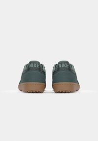 Green suede sneakers with a brown rubber sole, featuring Nike branding on the back and a smooth texture. Low-profile design.