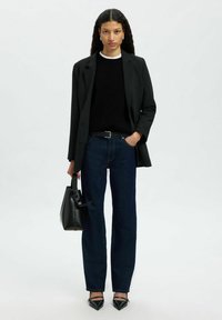 Svart kavaj över en svart tröja med vit krage, mörkblå raka jeans, svart väska och spetsiga svarta klackar. Texturerade tyger.