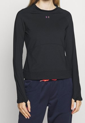 Mujer con una camiseta negra de manga larga de Under Armour con orificios para los pulgares y pantalones azul oscuro con un cordón rosa.