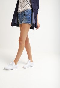 Světle modré džínové šortky s vybledlým efektem, doplněné vzorovaným topem a dlouhou námořnicky modrou košilí, doplněné bílými teniskami.