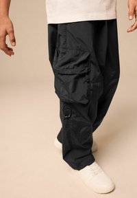 Svarta cargobyxor i lättviktigt material med flera fickor och elastiska muddar, kombinerade med vita sneakers. Enkel och funktionell design.