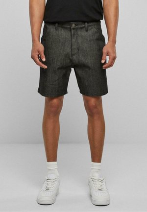 Pantalones cortos de mezclilla oscura con un diseño clásico, que cuentan con un cierre de botón, bolsillos y un corte recto. Llevados con zapatillas blancas y calcetines.