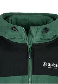 Black and green zippered jacket with fleece texture, featuring a high collar and adjustable hood. Logo on the left side.
